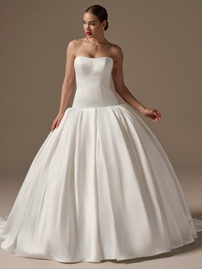 Model wearing the Adair wedding dress by Sottero and Midgley, featuring a sleek strapless bodice, structured corset construction, and dramatic full ball gown skirt in smooth satin.