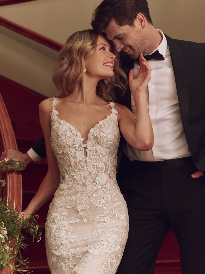 Close-up of lace fit-and-flare bridal gown with plunging neckline and floral appliqués, bride smiling at groom in a romantic wedding moment.