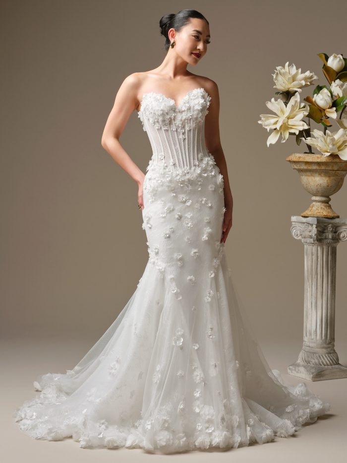 Akari fit and flare wedding dress featuring 3-D flowers with pearl accents over Chantilly lace, a sheer bodice with exposed boning and a basque waist, and a strapless sweetheart neckline.
