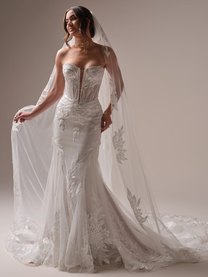 Bride wearing the Belladonna fit-and-flare wedding dress with plunging illusion sweetheart neckline, floral lace motifs, and sheer veil with botanical embroidery