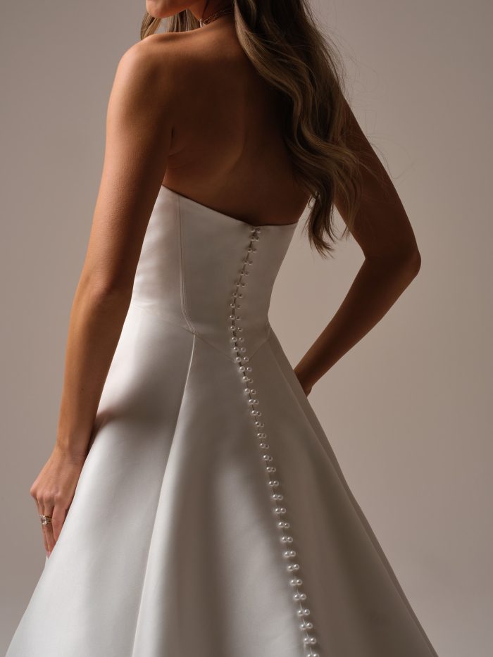 Back view of a strapless satin A-line wedding dress with covered pearl buttons trailing down the skirt, highlighting the smooth fabric and elegant silhouette.