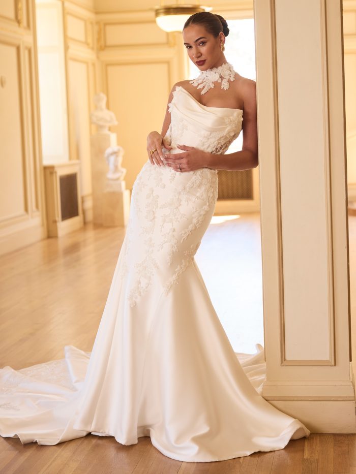 Bride wearing Burke by Sottero and Midgley, a strapless fit-and-flare satin bridal gown featuring a draped neckline, illusion corset details, and beaded lace appliqués trailing into a chapel-length train.