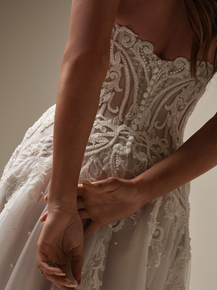Close-up back view of the Dharma wedding dress featuring an illusion bodice with exposed boning, intricate beaded lace details, scattered pearls, and covered button closure.