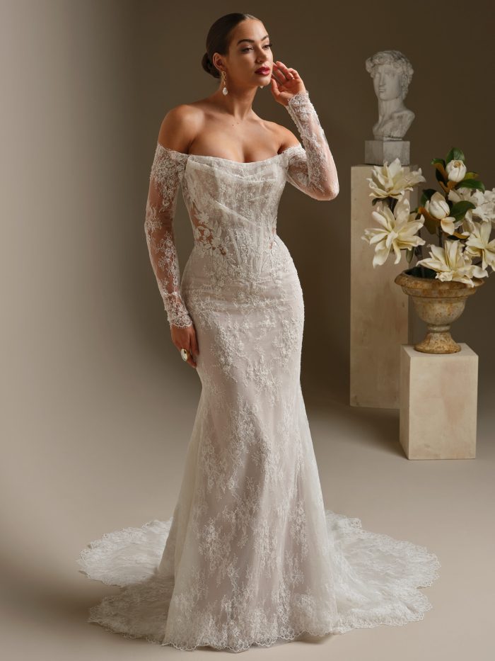 Dublin fit and flare wedding dress featuring beaded lace motifs over allover lace, an illusion bodice with a drop waist, off the shoulder lace sleeves, and a scalloped lace train.