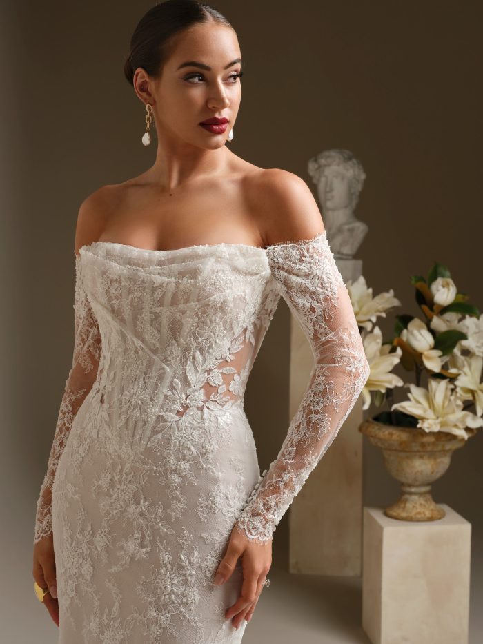 Close up of the Dublin wedding dress showing the draped illusion neckline, beaded lace motifs, sheer side details, and long off the shoulder lace sleeves.