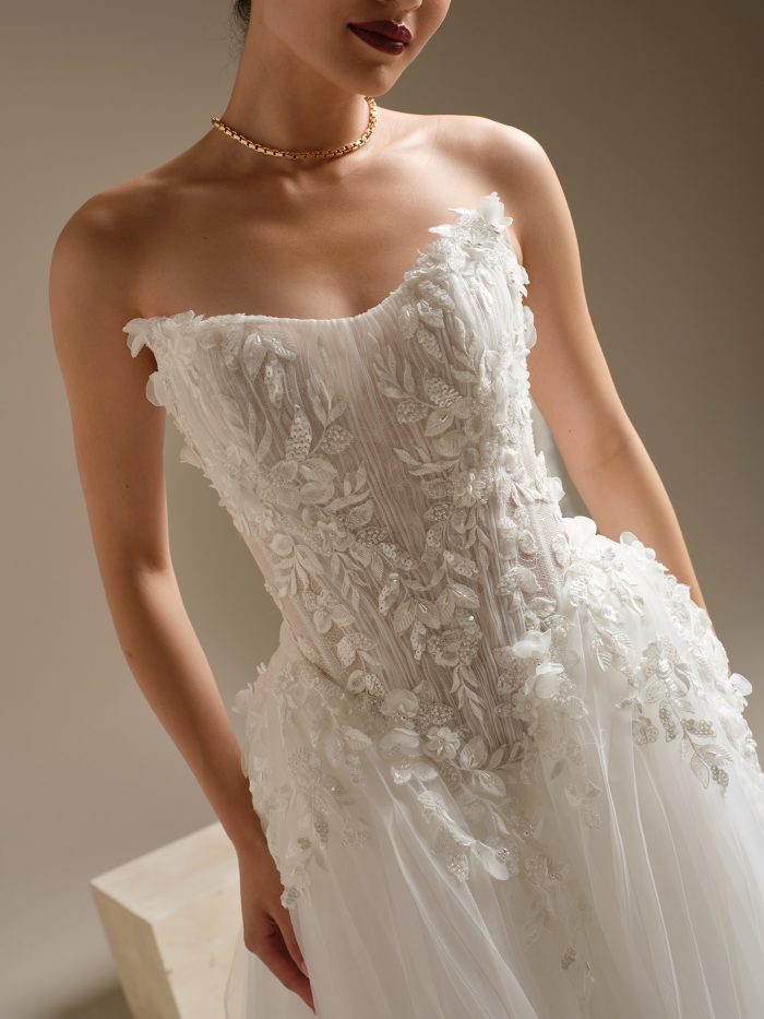 Close-up of the Jayna wedding dress by Sottero and Midgley, highlighting the sculpted cat-eye neckline, intricate 3-D floral beaded lace on the illusion bodice, and couture detailing at the basque waist.