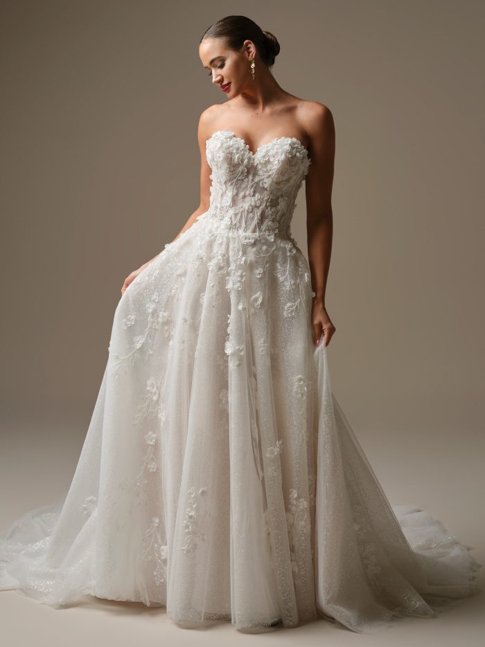 Bride wearing Kalinda by Sottero and Midgley, a strapless ball gown wedding dress with a sweetheart neckline, 3D floral appliqués, and layers of glitter tulle