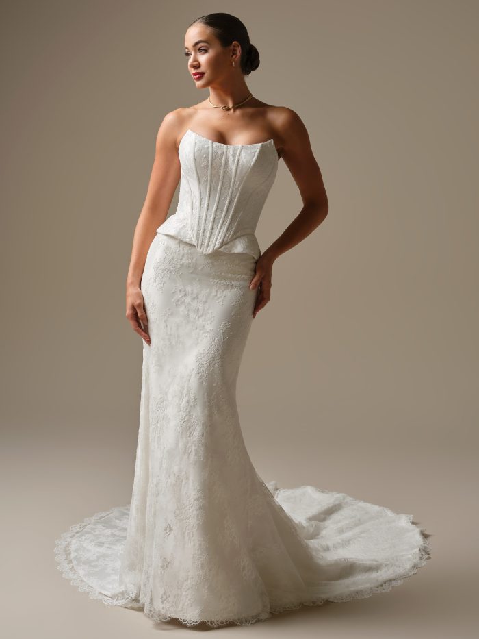 Bride wearing the Lassen strapless Chantilly lace wedding dress featuring a cat-eye neckline, corset bodice, peplum hips, and a fitted silhouette with a lace-trimmed train, photographed in a studio setting.
