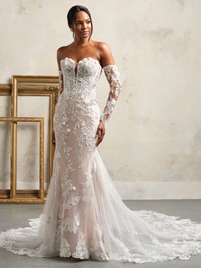 Bride wearing strapless fit-and-flare wedding dress with plunging neckline, illusion bodice, and embroidered lace appliqués over nude lining, styled with detachable lace sleeves and cathedral train.