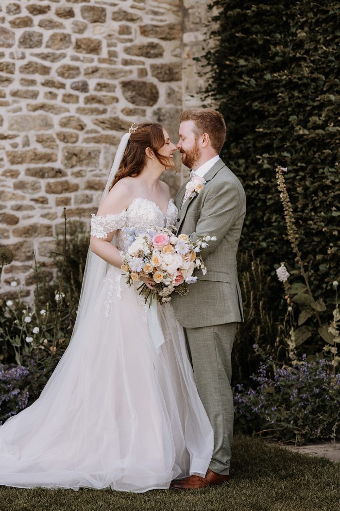 Bride wearing Stevie wedding dress by Maggie Sottero holding a peach fuzz-inspired bouquet with her husband.