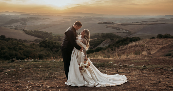 Bride wearing sparkly ballgown wedding dress in the arms of her groom in frontt of a scenic sunset