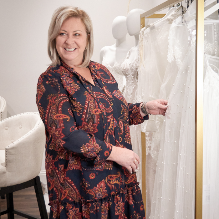 Women Owned Business Blog Header Of Maggie Sottero CEO Kelly Midgley In Front Of Maggie Sottero Wedding Dresses